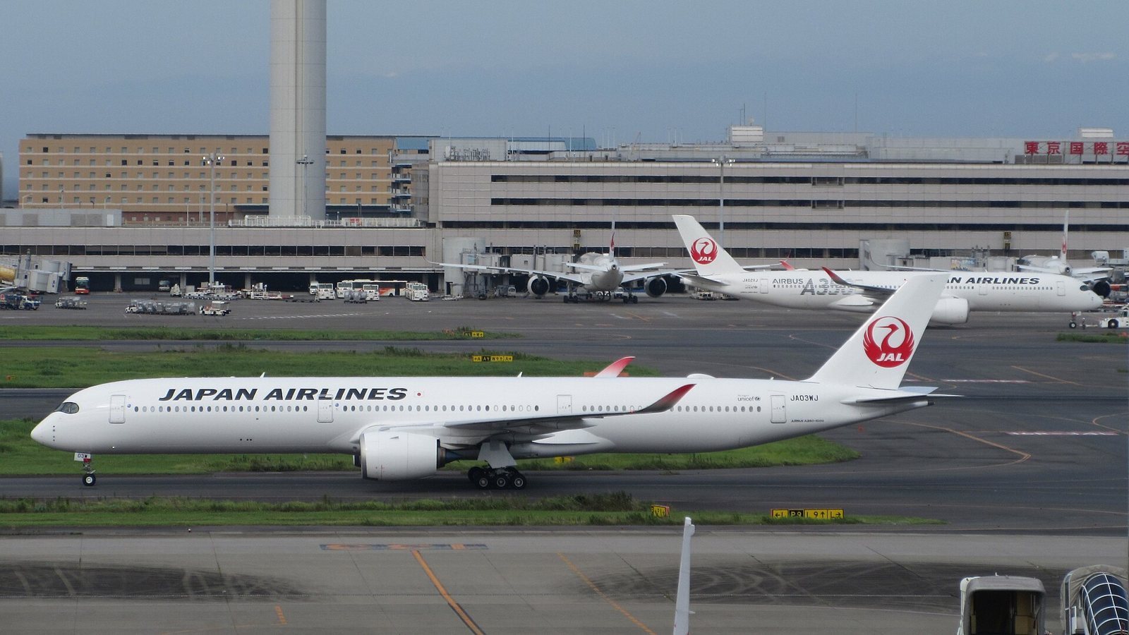 Un Airbus A350-1000 de Japan Airlines roule sur une voie de circulation, avec un A350-900 de la même compagnie à l’arrière-plan devant l’aérogare