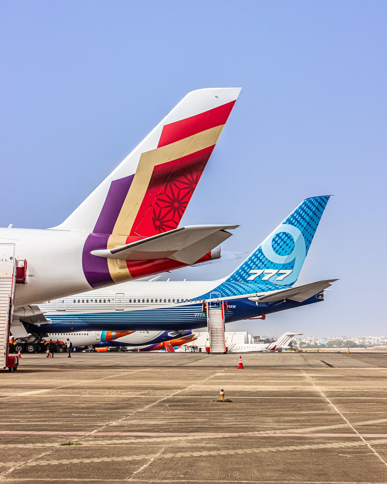 Les dérives d’un Airbus A350 d’Air India, aux motifs rouge, or et violet, et d’un Boeing 777-9 bleu marqué 777, côte à côte sur un tarmac
