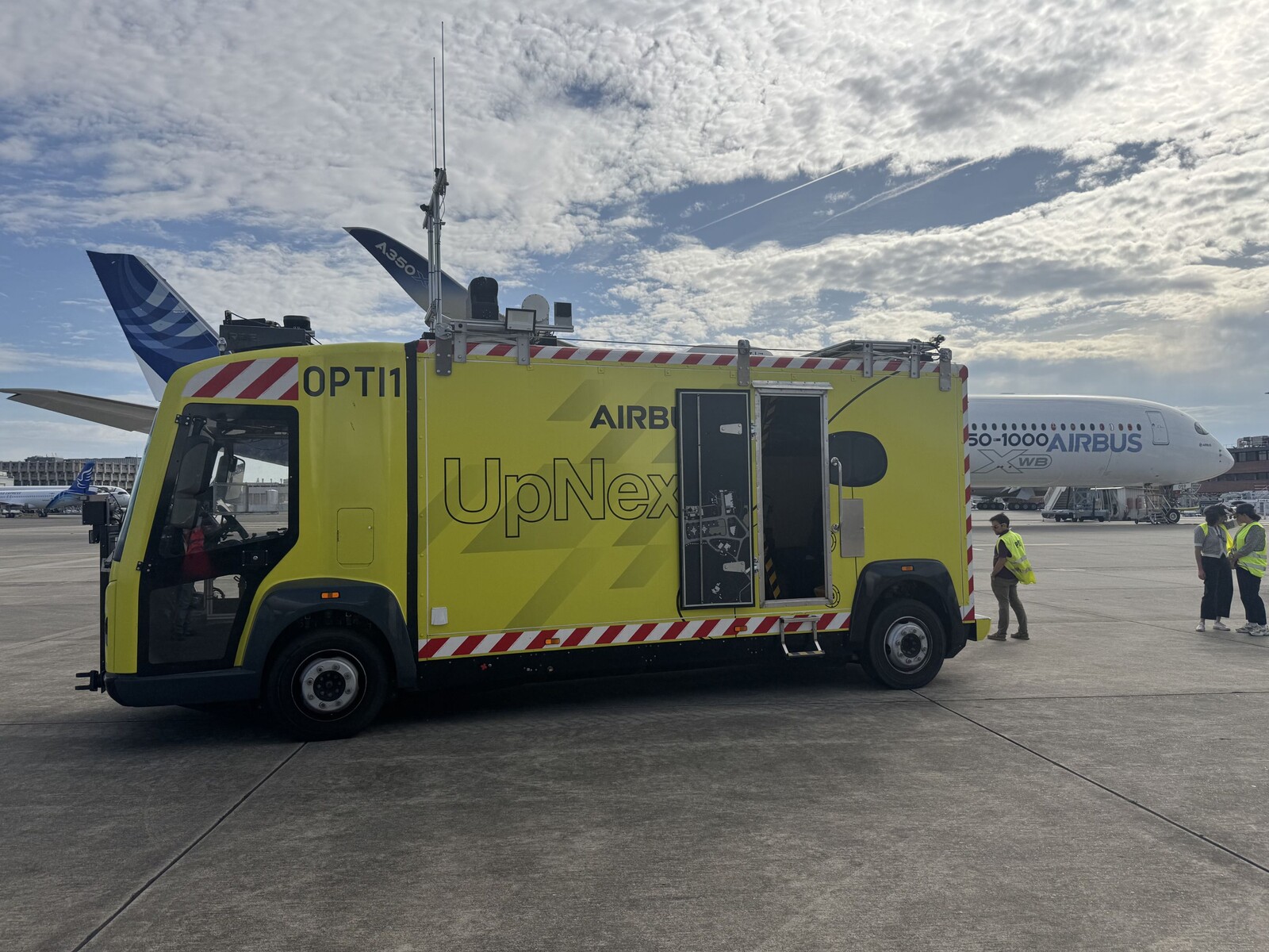 Le camion jaune OPTI1 d’Airbus UpNext stationné devant un A350-1000 sur le tarmac