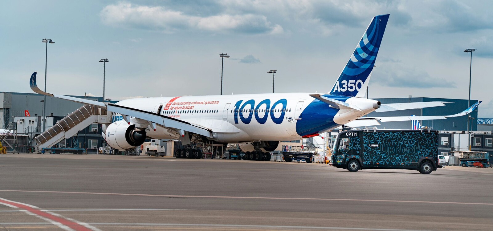 A350-1000 d’essais Airbus et fourgon noir OPTI1 UpNext sur le tarmac, hangars en fond