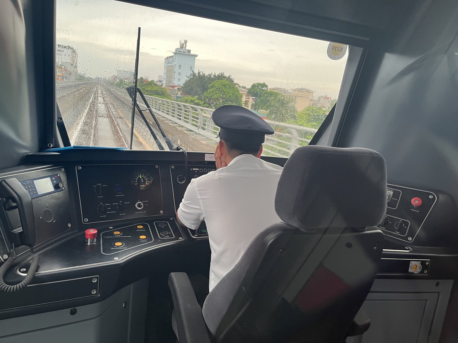 Un conducteur en chemise blanche et casquette, vu de dos dans la cabine d’une rame de la ligne 3, face à la voie aérienne qui file vers la ville