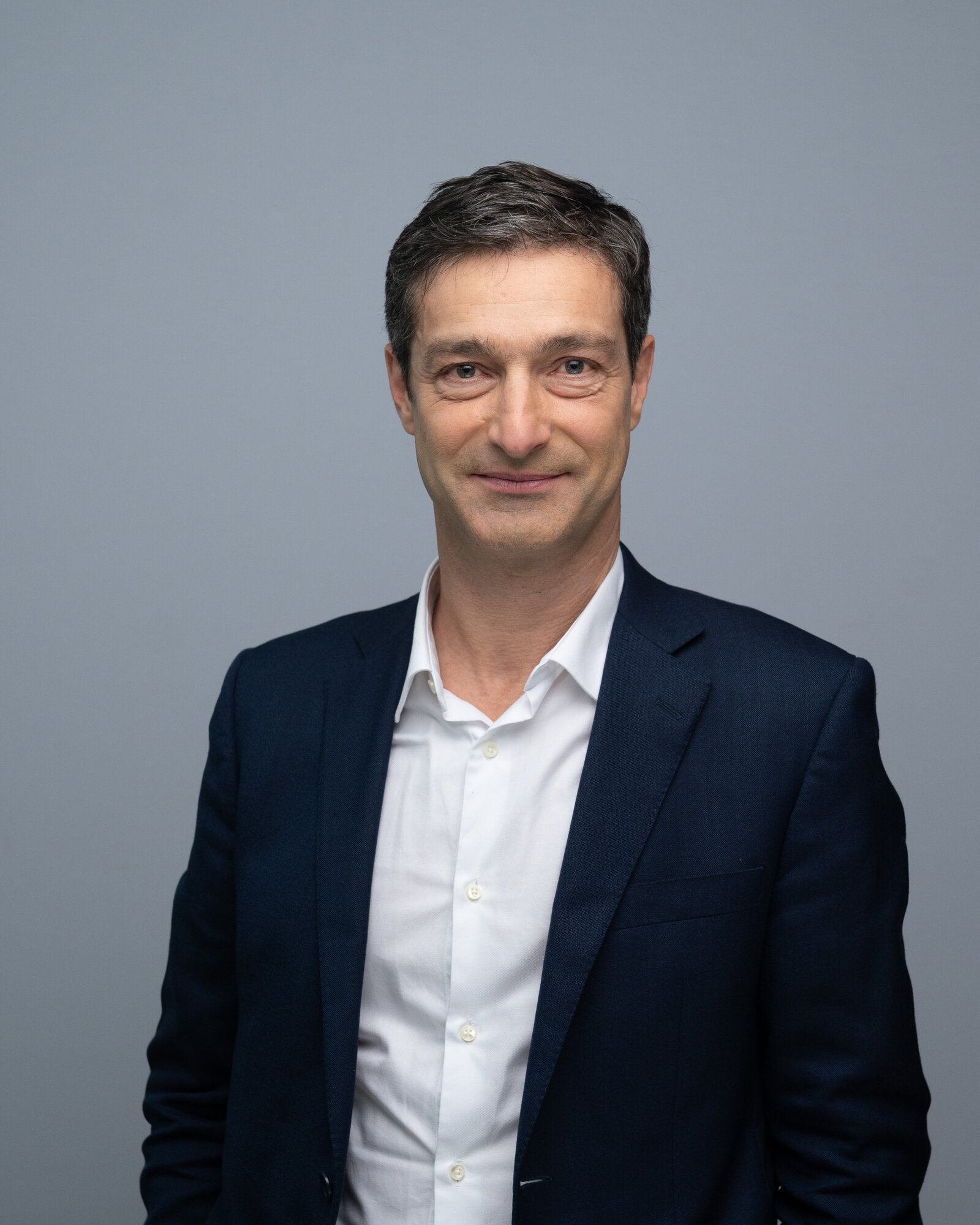 Pierre Villeroy de Galhau souriant, en veste sombre et chemise blanche, sur fond gris