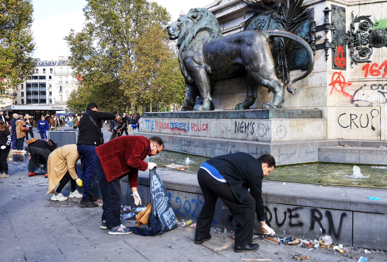Des habitants, sacs-poubelle à la main, ramassent les déchets au pied du lion de la statue de la République, couverte de tags