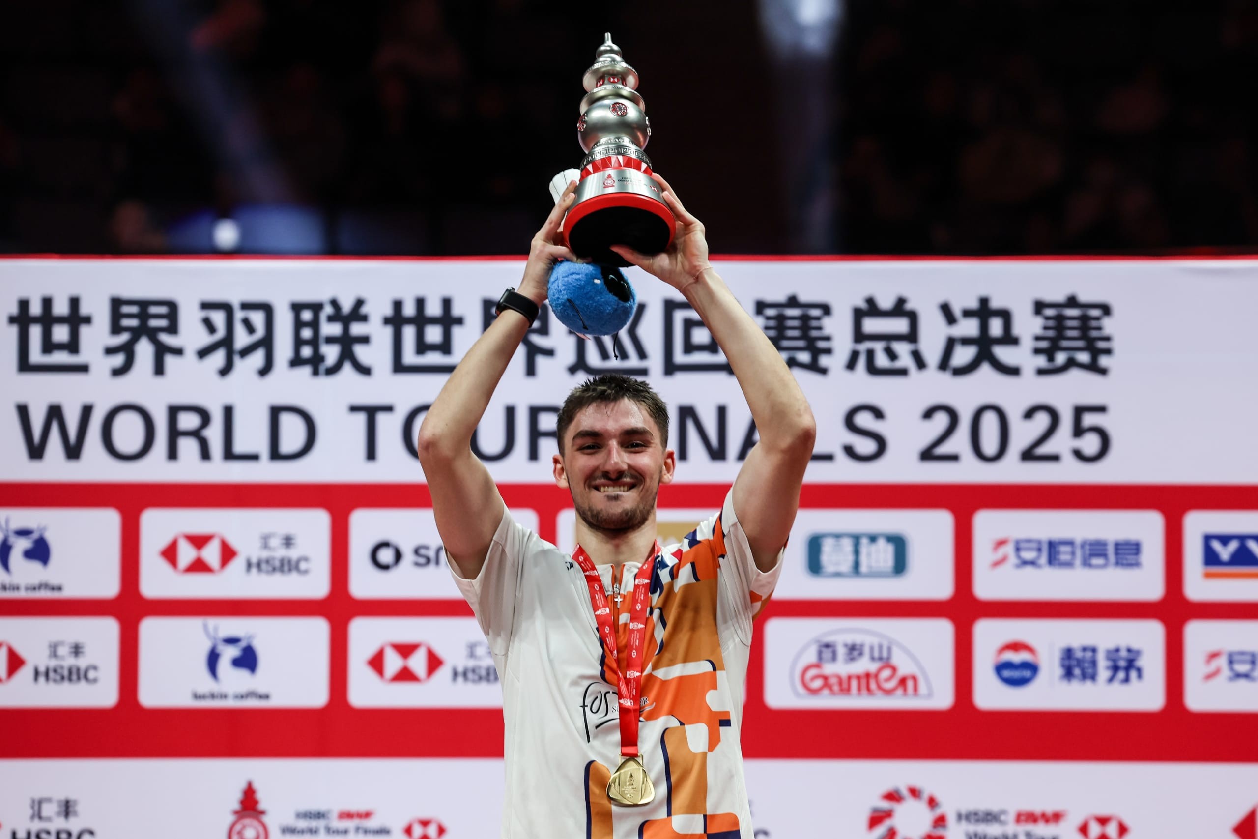 Christo Popov, médaille autour du cou, brandit un grand trophée argenté devant un panneau des World Tour Finals 2025