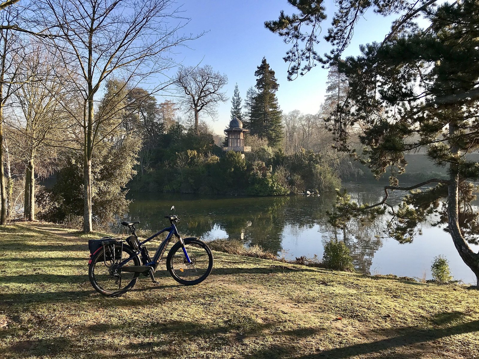 Vélo électrique noir garé au bord d’un lac dans le bois de Boulogne, arbres en arrière-plan