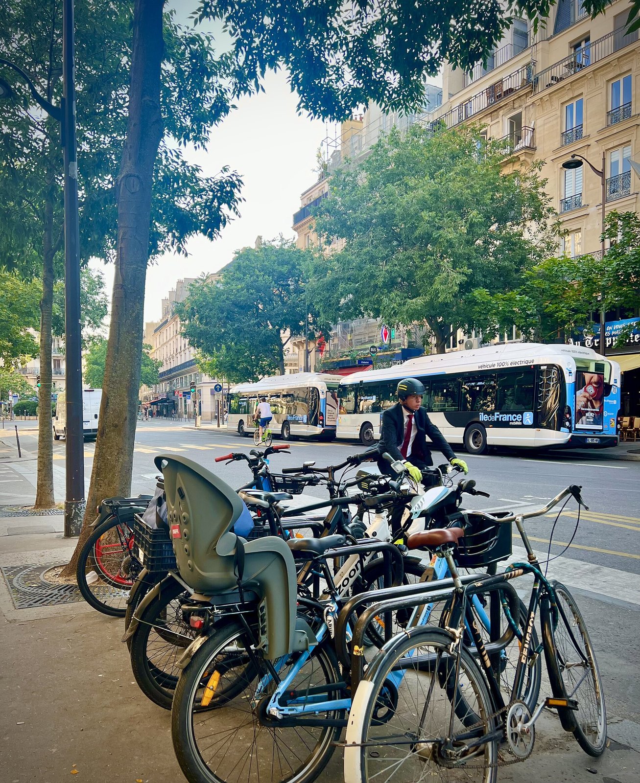 Vélos garés contre des arceaux sur un trottoir parisien, bus électrique blanc et vert en arrière-plan