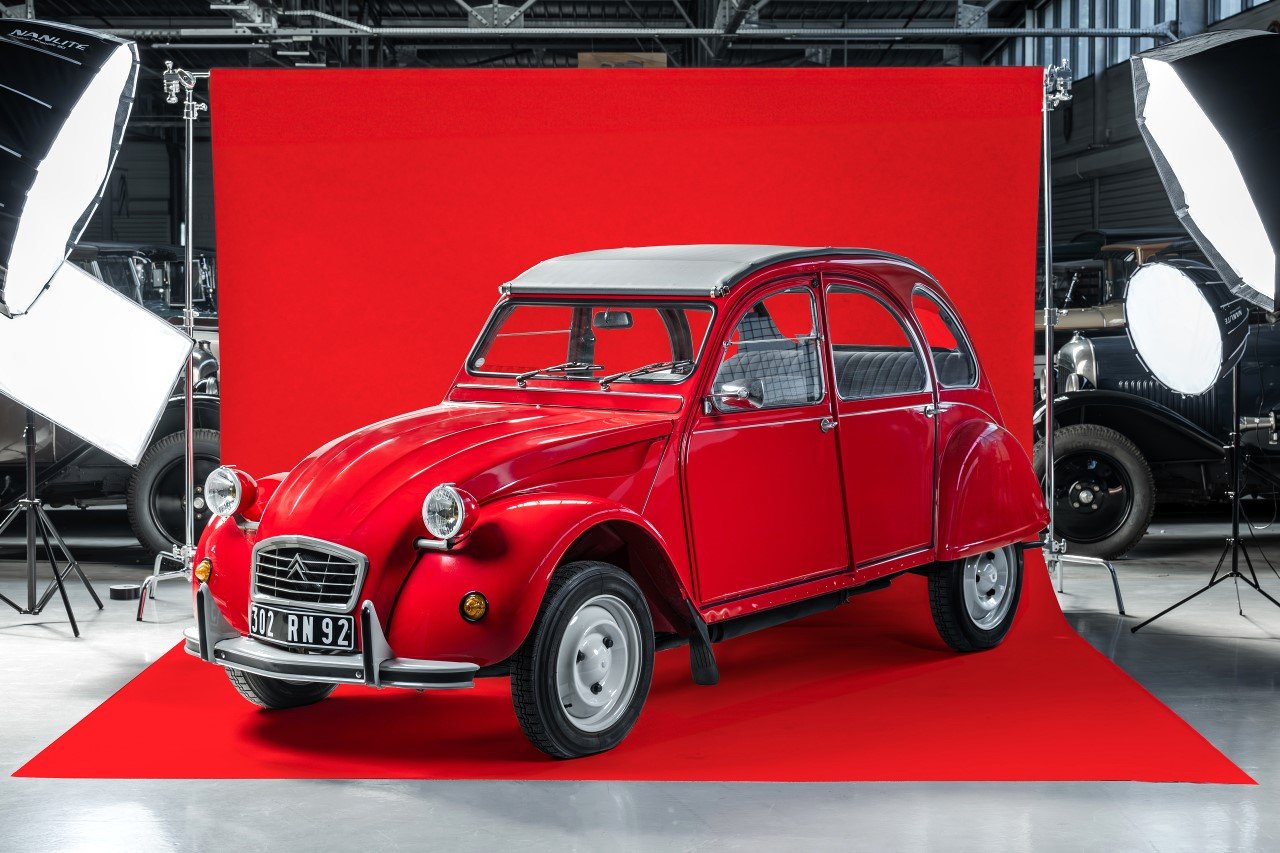 Une Citroën 2CV rouge d’origine photographiée en studio devant un fond rouge
