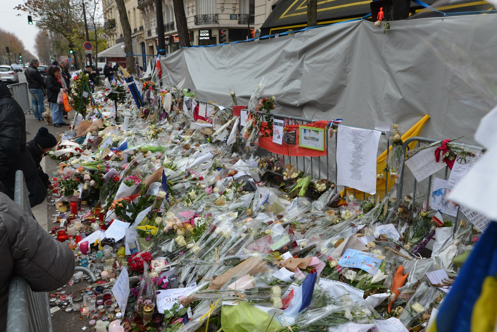 Des passants devant un long mémorial de fleurs, de bougies et de messages déposés devant le Bataclan