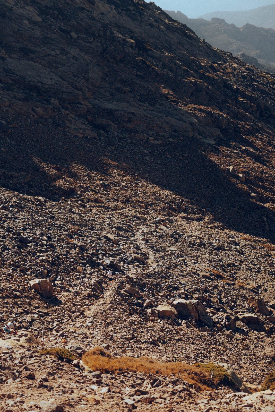 Sentier de pierres serpentant sur un versant aride du GR20, montagnes corses à l’arrière-plan