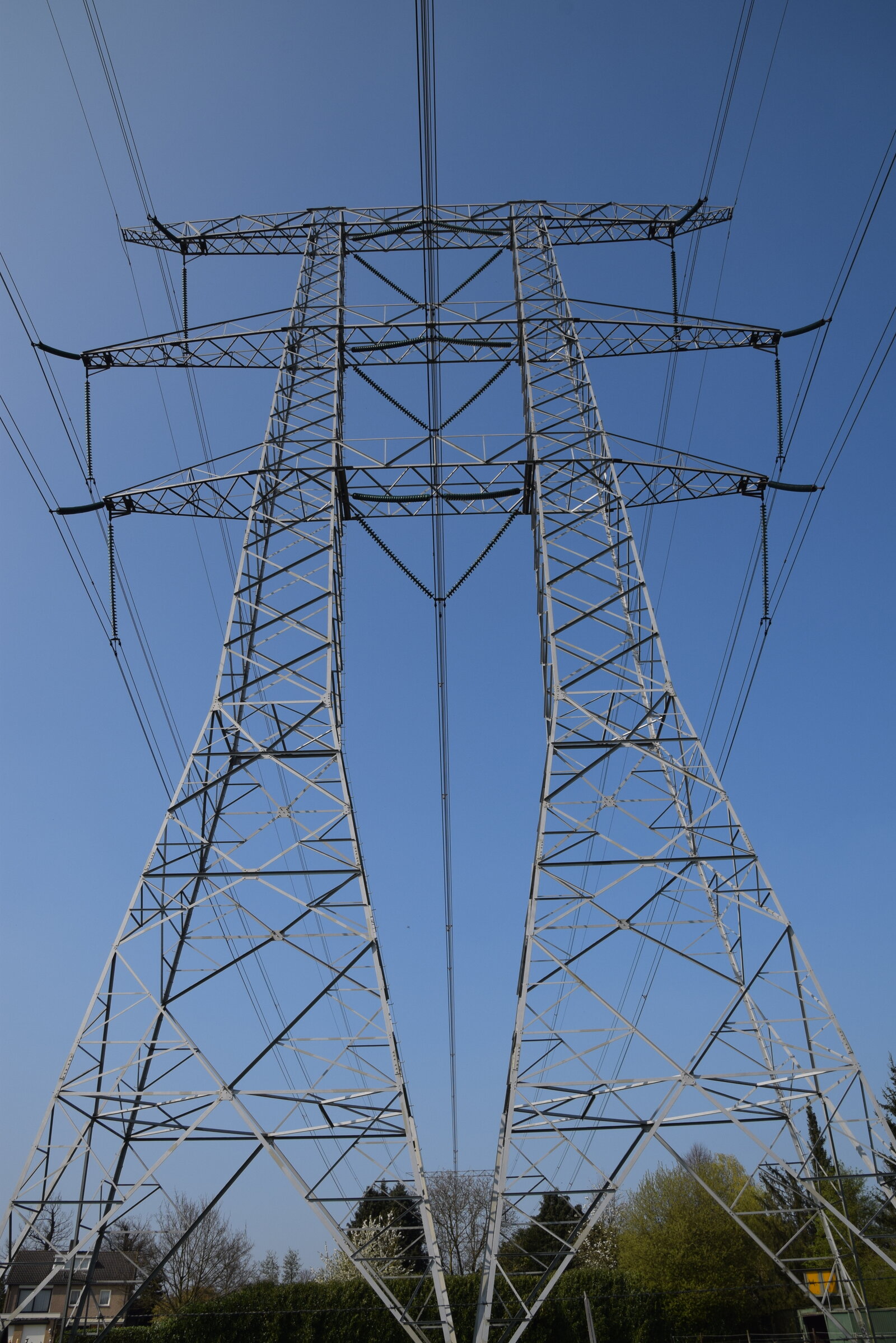 Un double pylône électrique en treillis métallique vu du sol, sous un ciel bleu