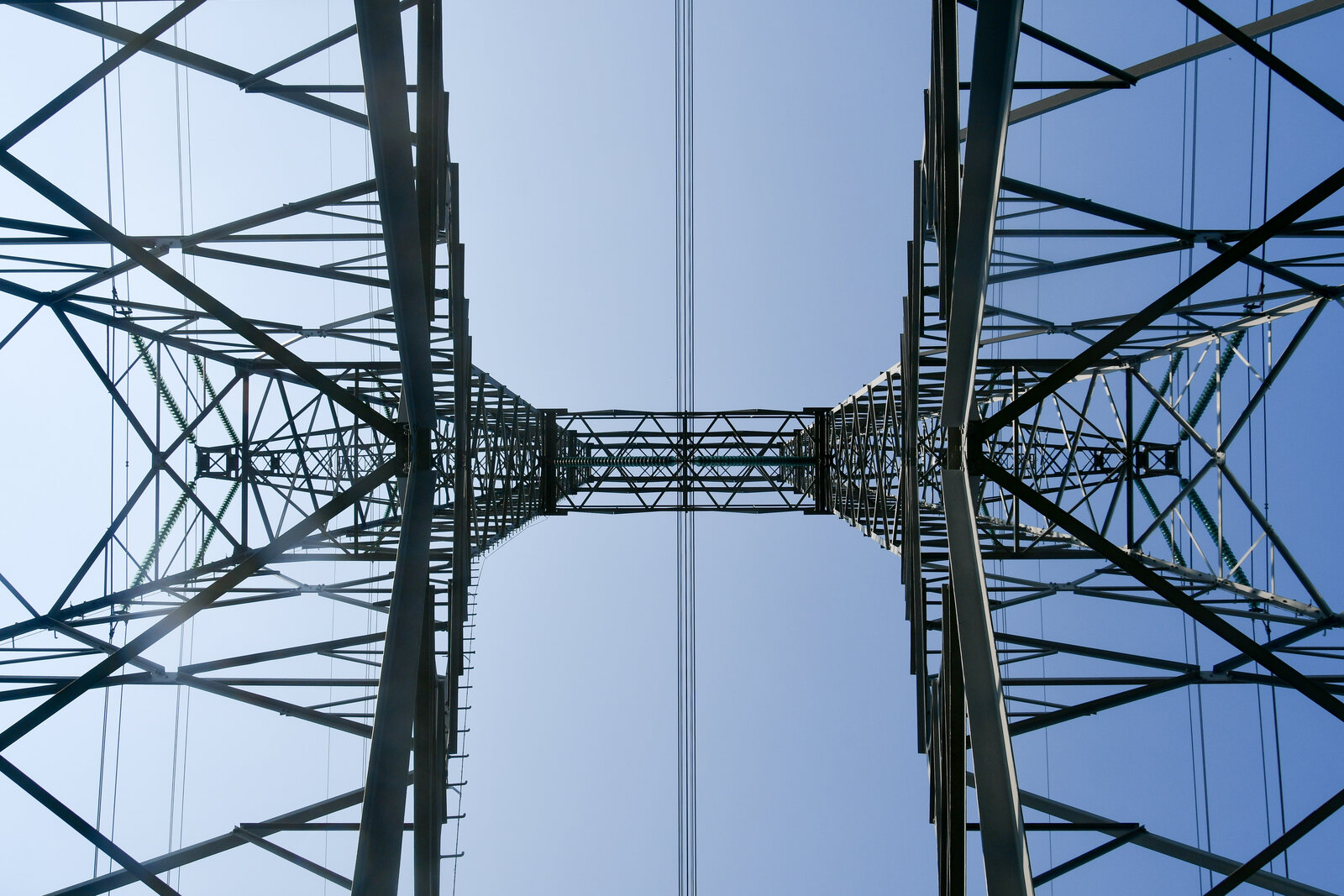 Vue en contre-plongée depuis le pied d’un pylône haute tension, dont les deux montants en treillis se rejoignent dans le ciel