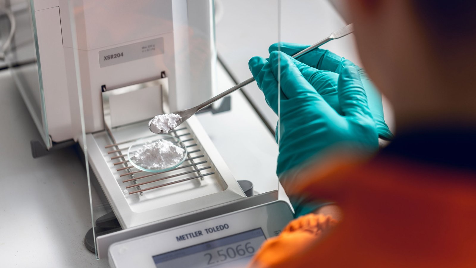 Une chercheuse en gants pèse un échantillon sur une balance de précision dans un laboratoire