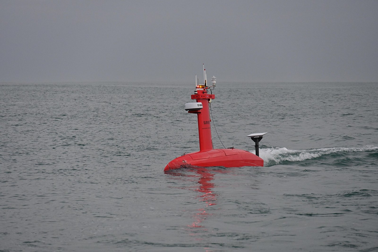 Drone de surface DriX rouge naviguant sur une mer grise, mât d’antennes visible