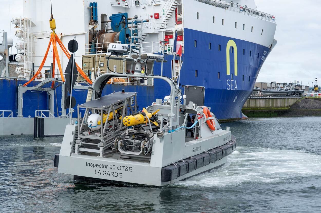 Drone de surface Inspector gris immatriculé La Garde, manœuvrant dans un port près d’un grand navire bleu