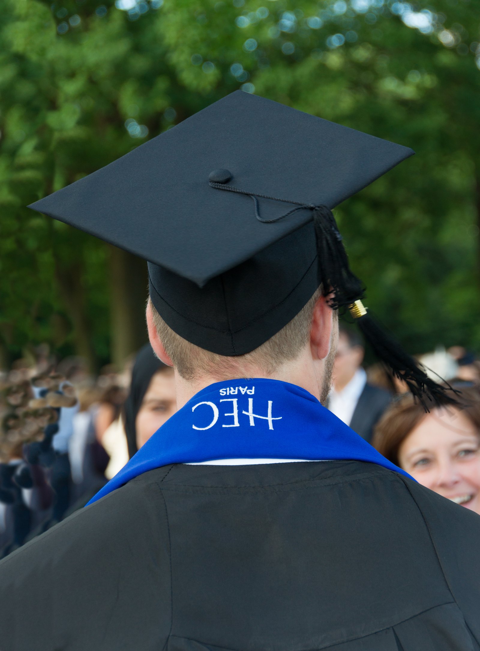 Un diplômé d’HEC Paris en toge et toque, une écharpe bleue HEC sur les épaules, devant une proche souriante