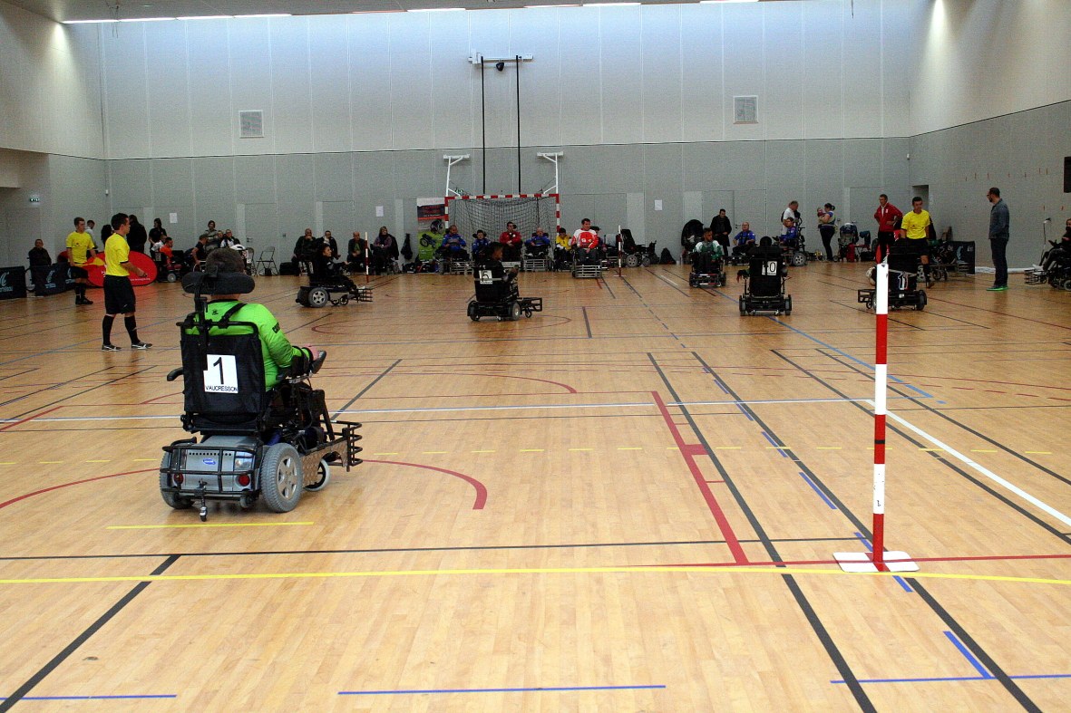 Un joueur en fauteuil électrique, maillot vert et numéro 1, sur le parquet d’un gymnase pendant un match du championnat de France