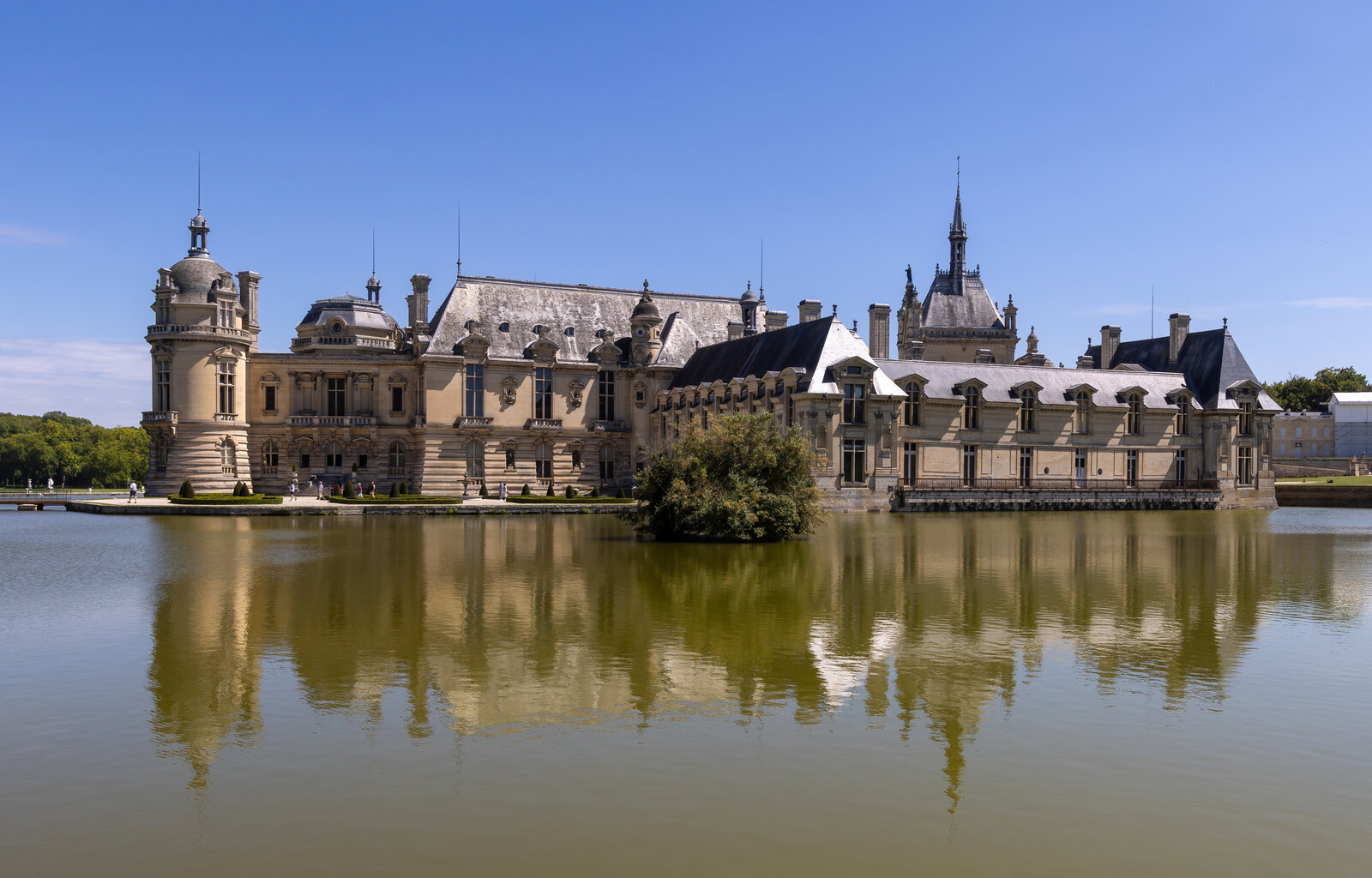 Le château de Chantilly vu de côté, reflété dans l’eau des douves sous un ciel clair