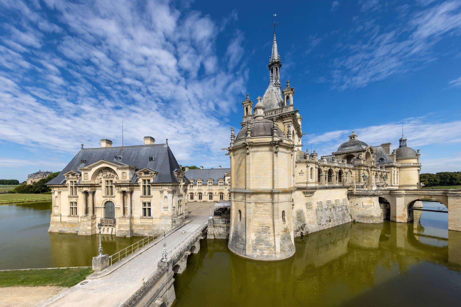 Pont menant au château de Chantilly, façades et tours sous un ciel bleu