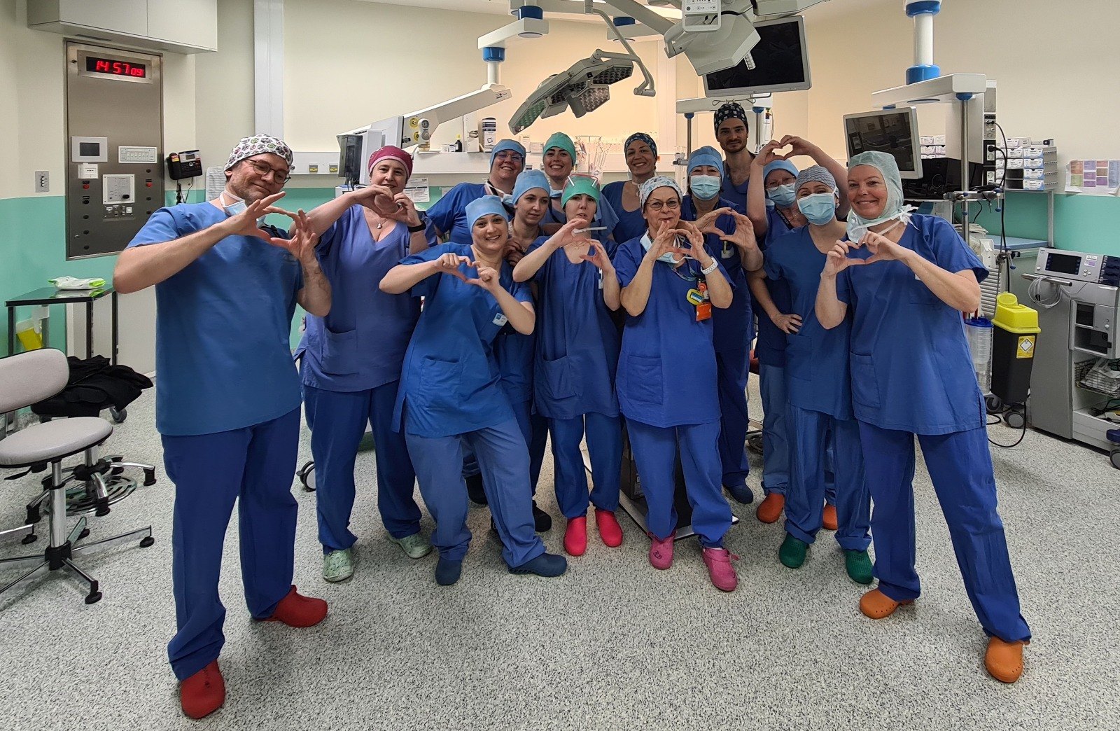 Une quinzaine de soignants en tenue de bloc forment un cœur avec leurs mains dans une salle d’opération de l’hôpital Femme Mère Enfant