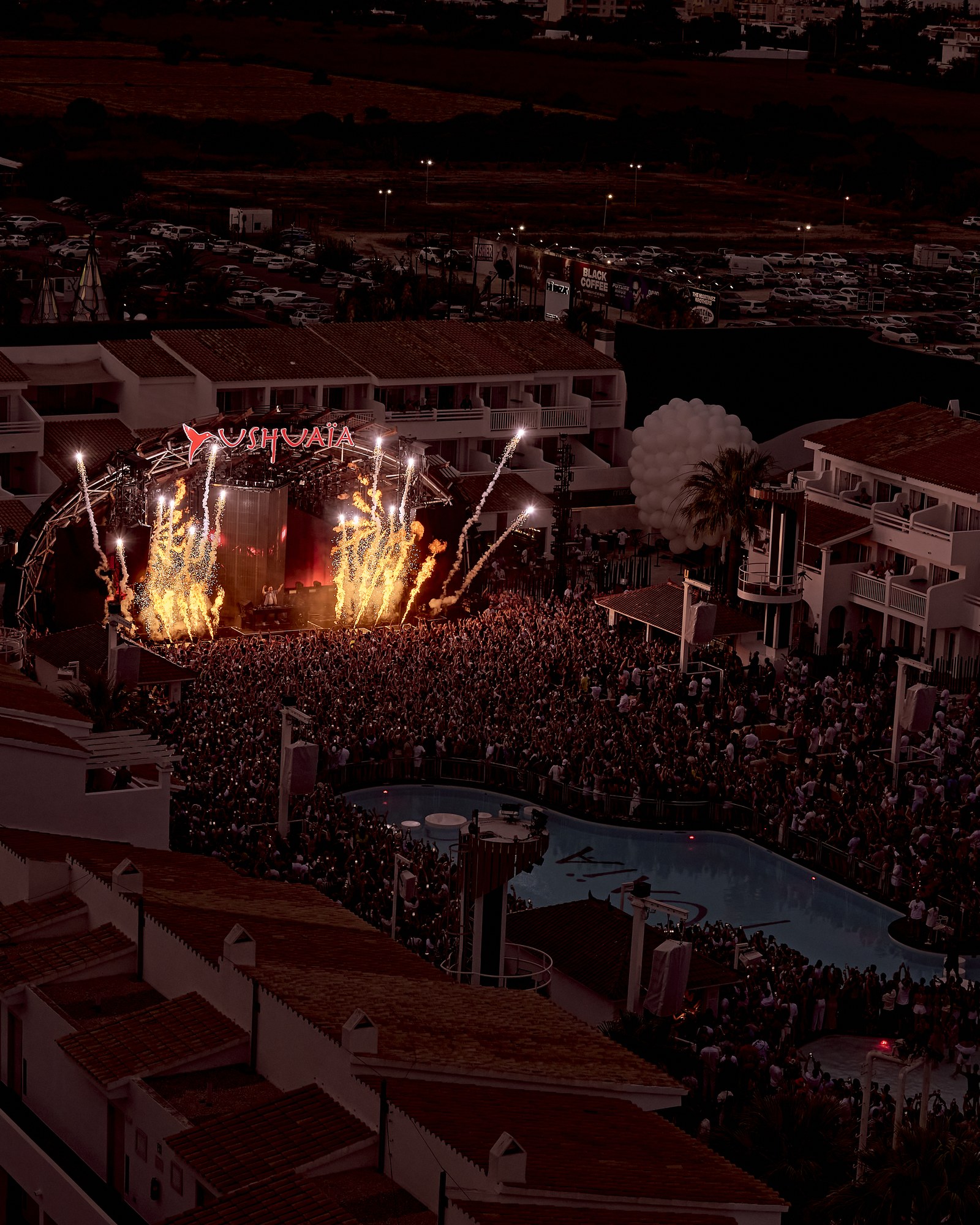 Vue d’ensemble du club Ushuaïa à Ibiza de nuit, scène illuminée et foule massée autour de la piscine