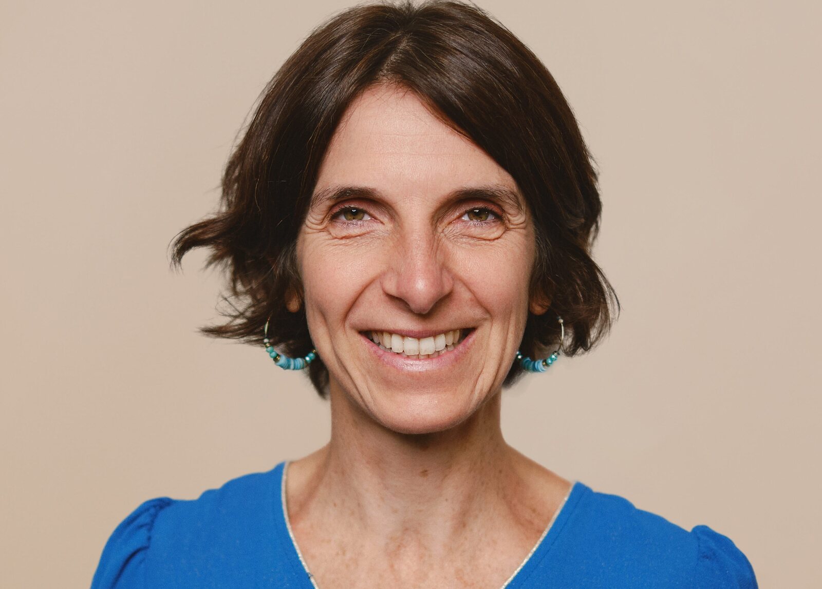 Portrait de Sophie Brac de la Perrière, cheveux bruns courts et boucles d’oreilles turquoise, souriant largement