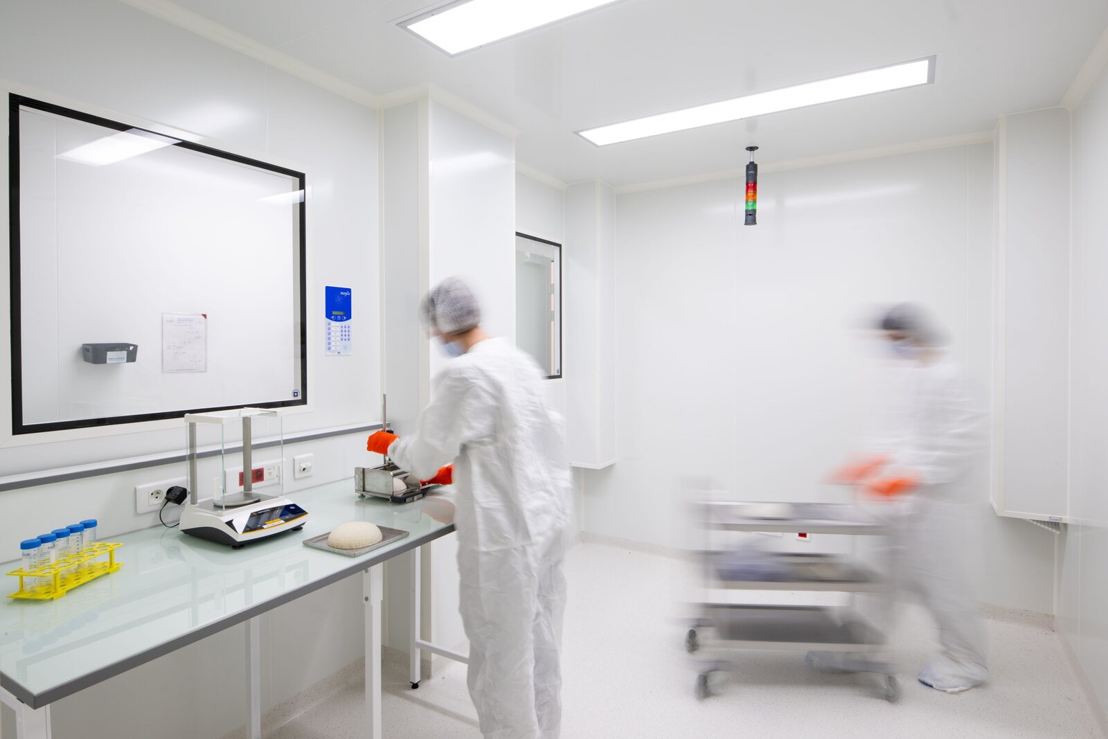 Deux techniciens en combinaison blanche, charlotte et masque, travaillent dans une salle blanche lumineuse