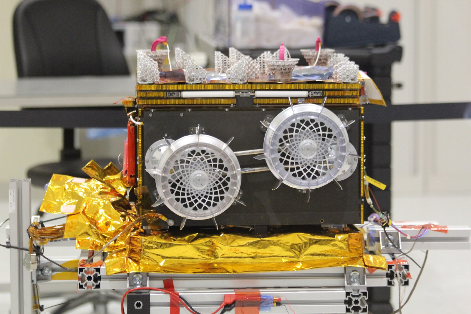 Le rover Idefix replié, boîtier noir aux bords dorés, avec ses deux roues ajourées visibles sur le côté, posé sur son support en salle d’intégration