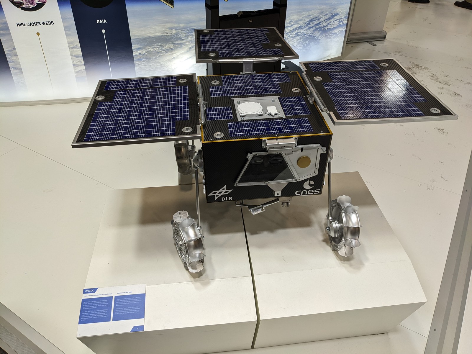 Maquette du rover Idefix, panneaux solaires déployés et roues sorties, exposée sur un socle blanc, avec les logos du CNES et du DLR