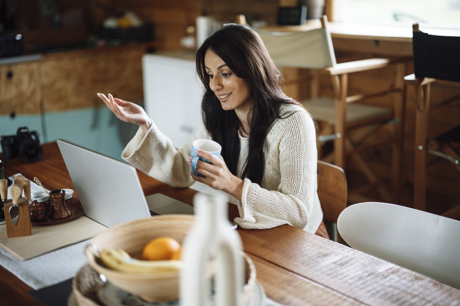 Une femme assise à une table parle tout en consultant un ordinateur portable