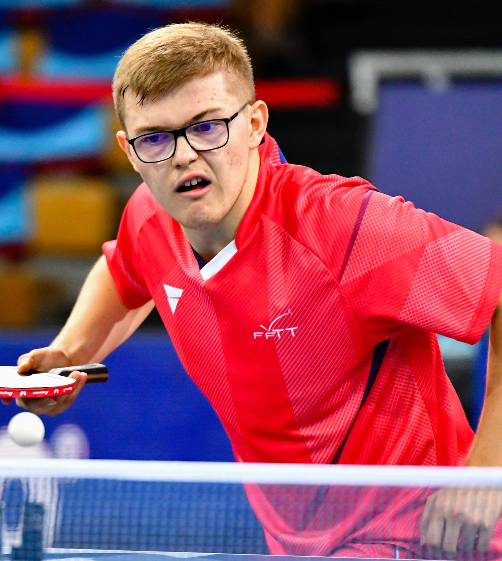 Portrait d’Alexis Lebrun en maillot rouge FFTT, regard fixé sur la balle