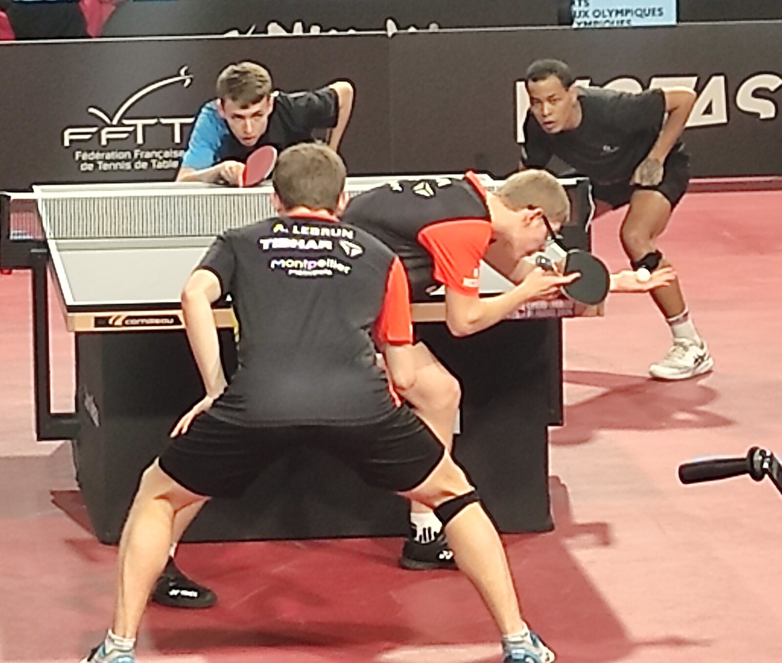 Alexis et Félix Lebrun, dos à l’objectif, maillots noirs et oranges, prêts à servir face à leurs adversaires