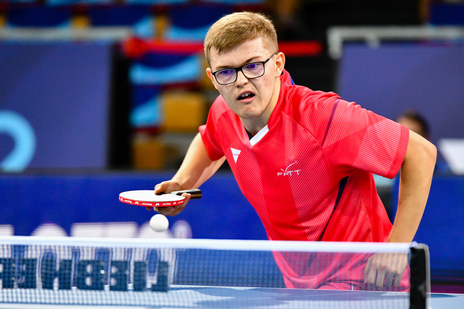 Alexis Lebrun penché au-dessus de la table, raquette horizontale, balle qui rebondit devant lui