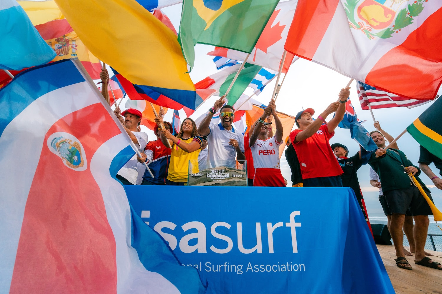 Des surfeurs de nombreux pays brandissent leurs drapeaux sous une banderole de l’ISA lors de la cérémonie d’ouverture