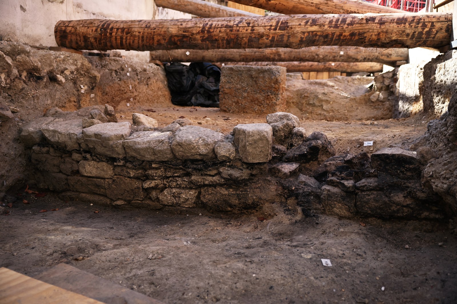 Le mur gaulois de l’Hôtel-Dieu, assise de grosses pierres sèches noircies, au fond de la fouille sous de lourds étais en bois