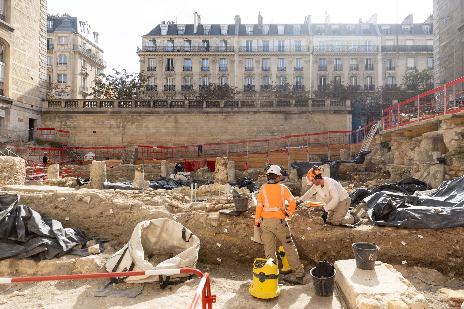 La cour de fouille de l’Hôtel-Dieu, avec deux archéologues au travail au premier plan et les immeubles haussmanniens de l’île de la Cité au fond