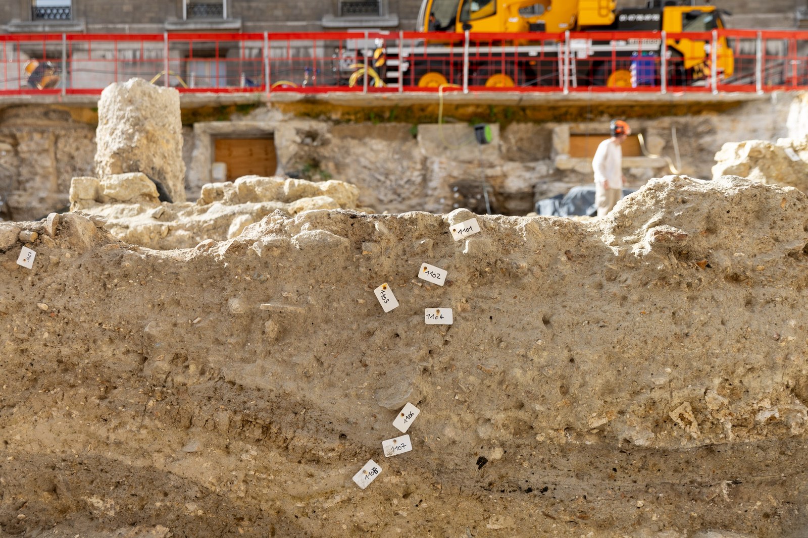 Une coupe de terrain stratifiée parsemée d’étiquettes blanches, au pied des barrières rouges du chantier de l’Hôtel-Dieu