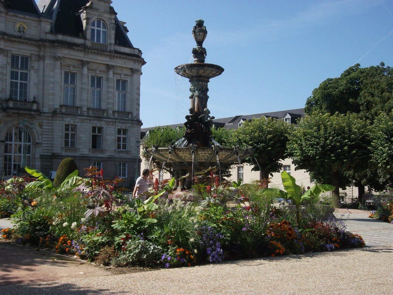 La fontaine de la place de l’hôtel de ville de Limoges entourée de massifs fleuris, sous un ciel bleu