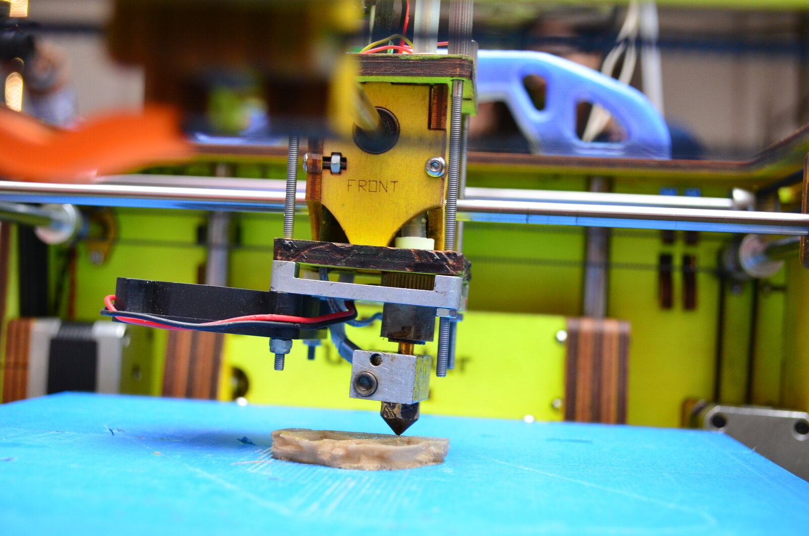 Gros plan sur la buse d’une imprimante 3D qui dépose de la matière couche par couche sur un plateau bleu