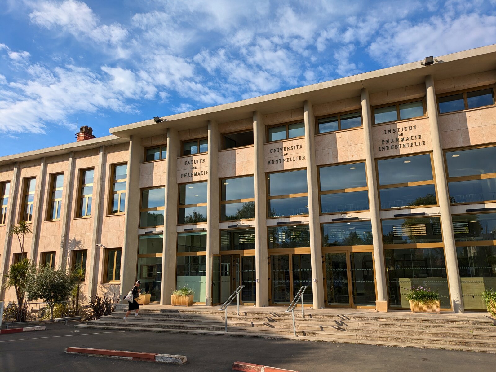 La façade vitrée et l’escalier d’entrée de la faculté de pharmacie de Montpellier sous un ciel bleu