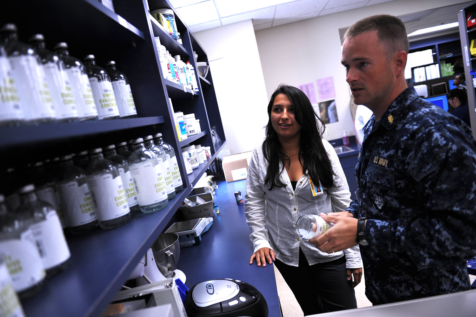 Un pharmacien en uniforme montre des flacons à une lycéenne dans les rayonnages d’une pharmacie d’hôpital