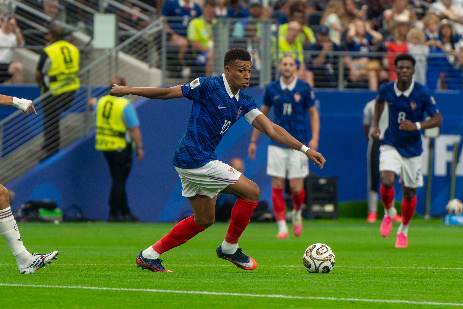 Kylian Mbappé accélère balle au pied, bras écartés, devant un adversaire