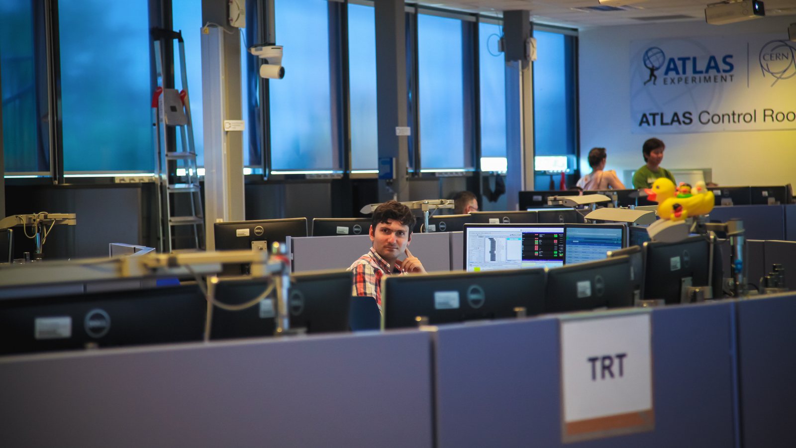 Un jeune chercheur, assis seul devant plusieurs écrans, travaille dans la salle de contrôle de l’expérience ATLAS