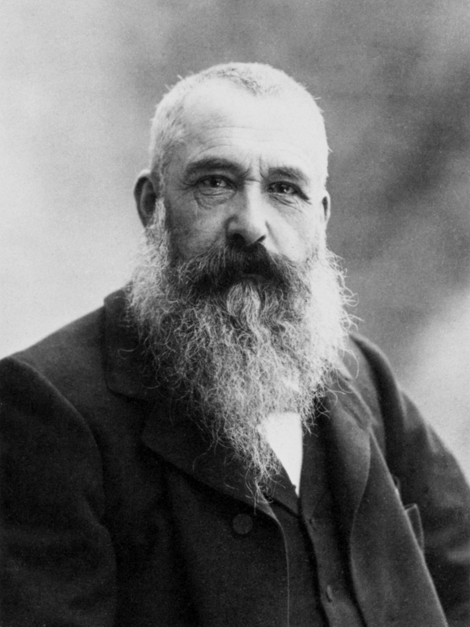 Portrait en noir et blanc de Claude Monet à 58 ans, longue barbe blanche, regard droit vers l’objectif, en veste sombre