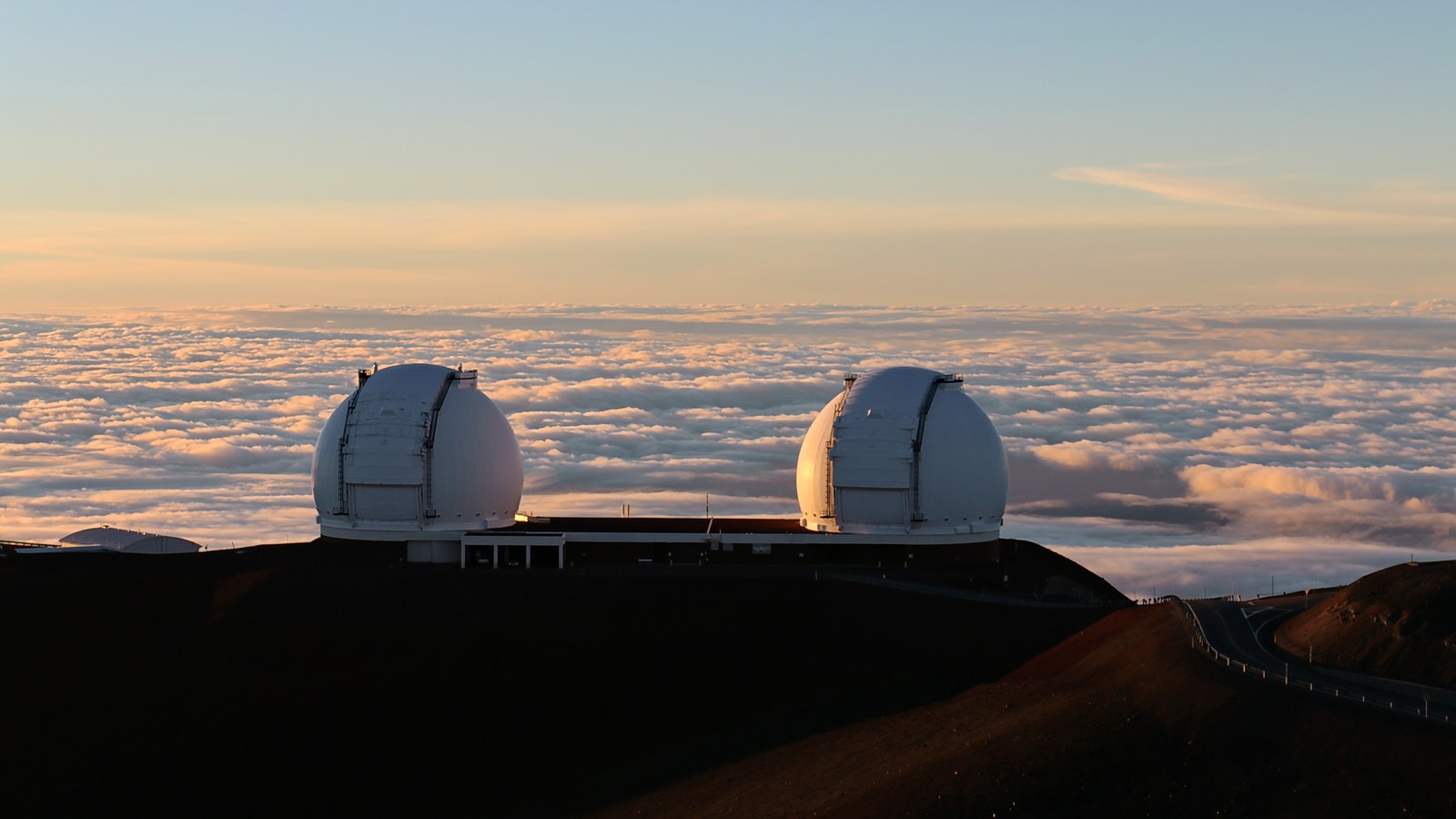Les deux coupoles blanches des télescopes Keck au sommet du Mauna Kea, au-dessus d’une mer de nuages au coucher du soleil