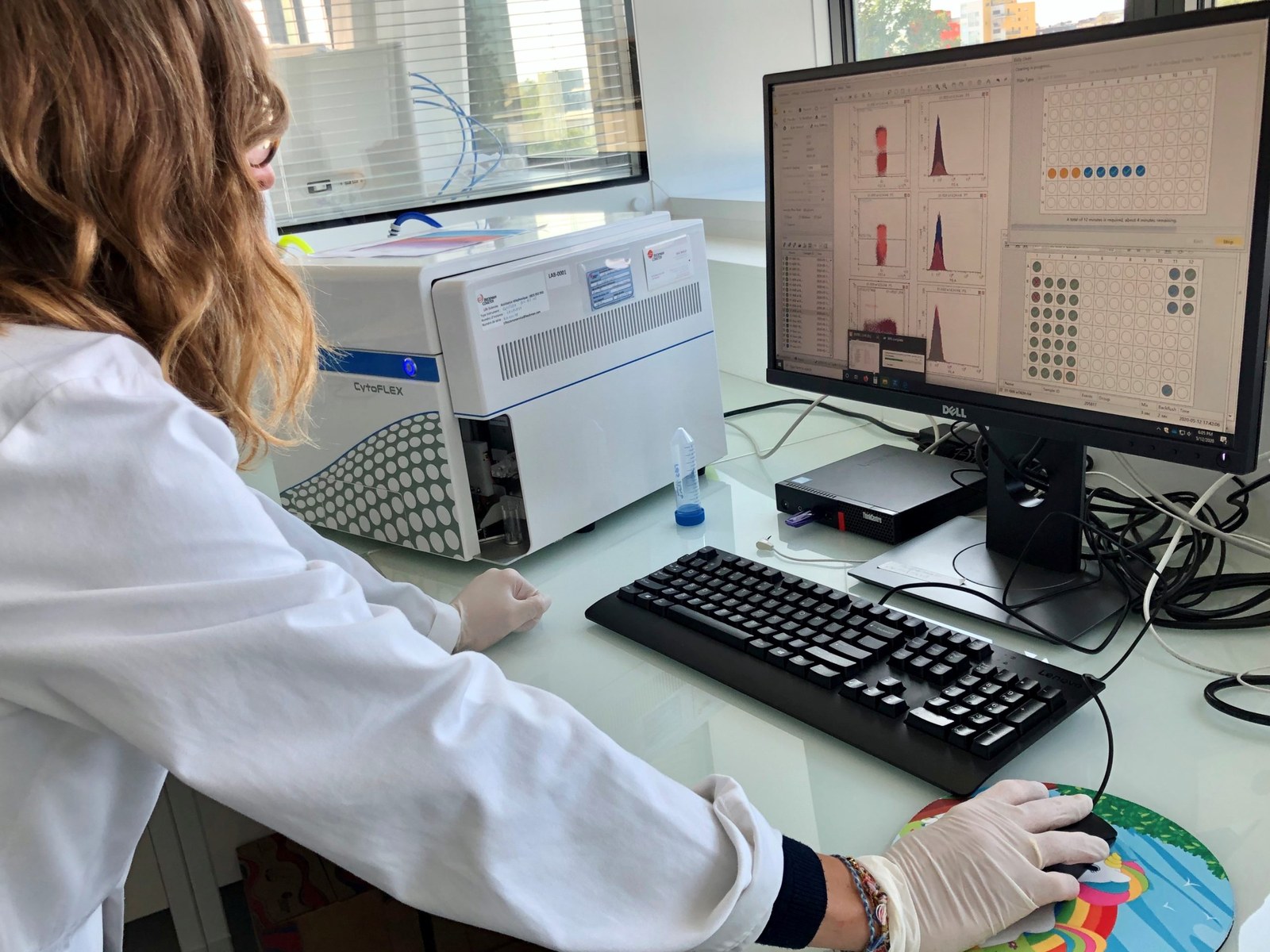 Une chercheuse en blouse et gants analyse des résultats sur un écran d’ordinateur dans un laboratoire