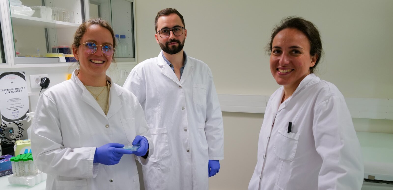 Gwendoline Tallec, gants bleus, tient une lame de laboratoire, à côté d’Antoine Droneau et d’Hélène Malka-Mahieu, tous trois souriants en blouse blanche