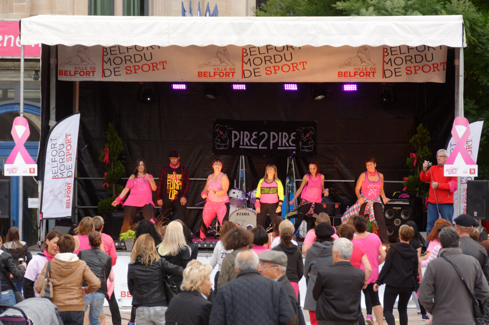 Des participantes en tee-shirt rose sur une scène et une foule devant elles, lors d’une animation Octobre rose à Belfort