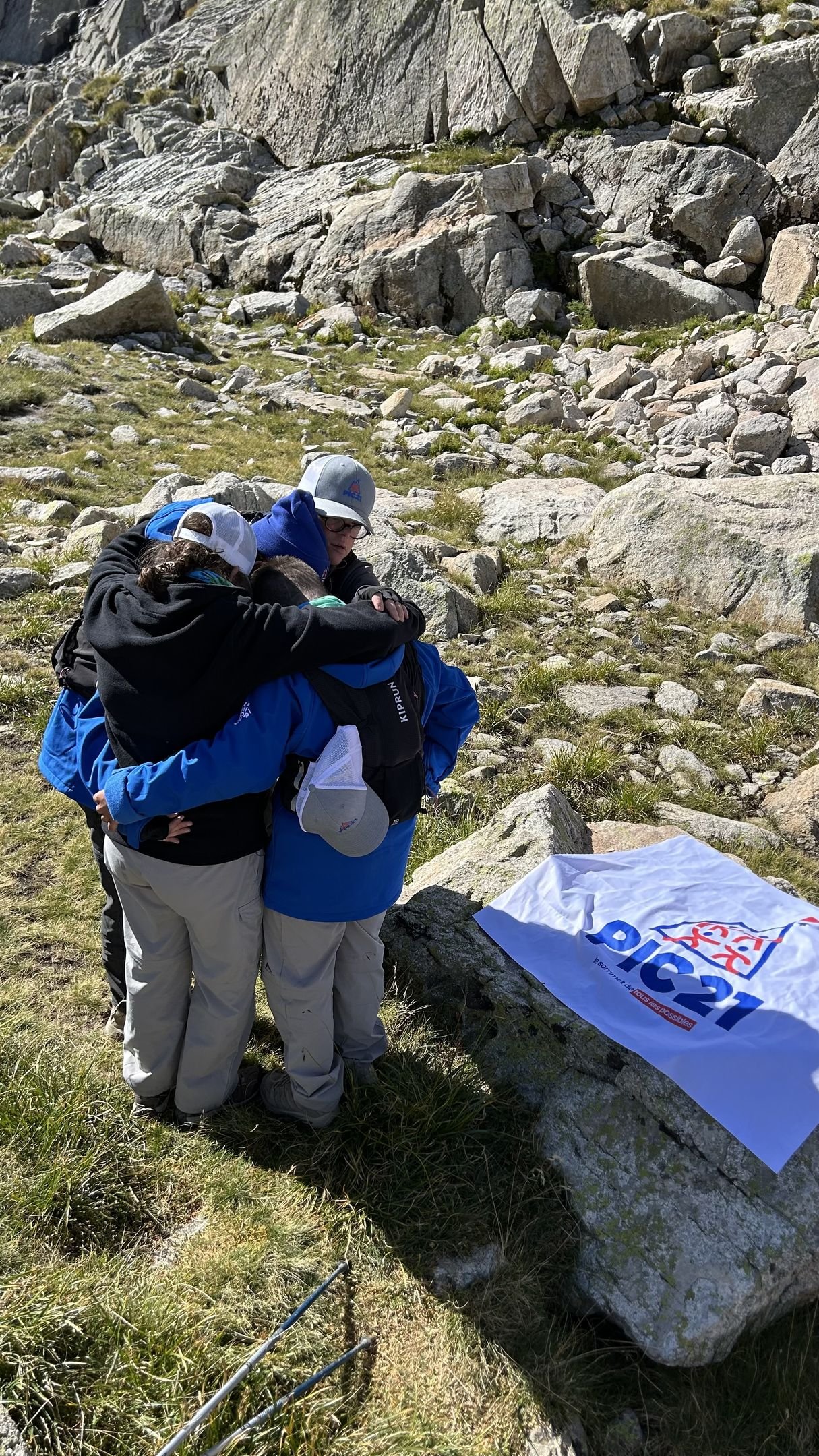 Deux randonneurs de dos, sacs sur les épaules, face à une pente rocheuse, à côté d’un drapeau Pic 21 posé sur les rochers