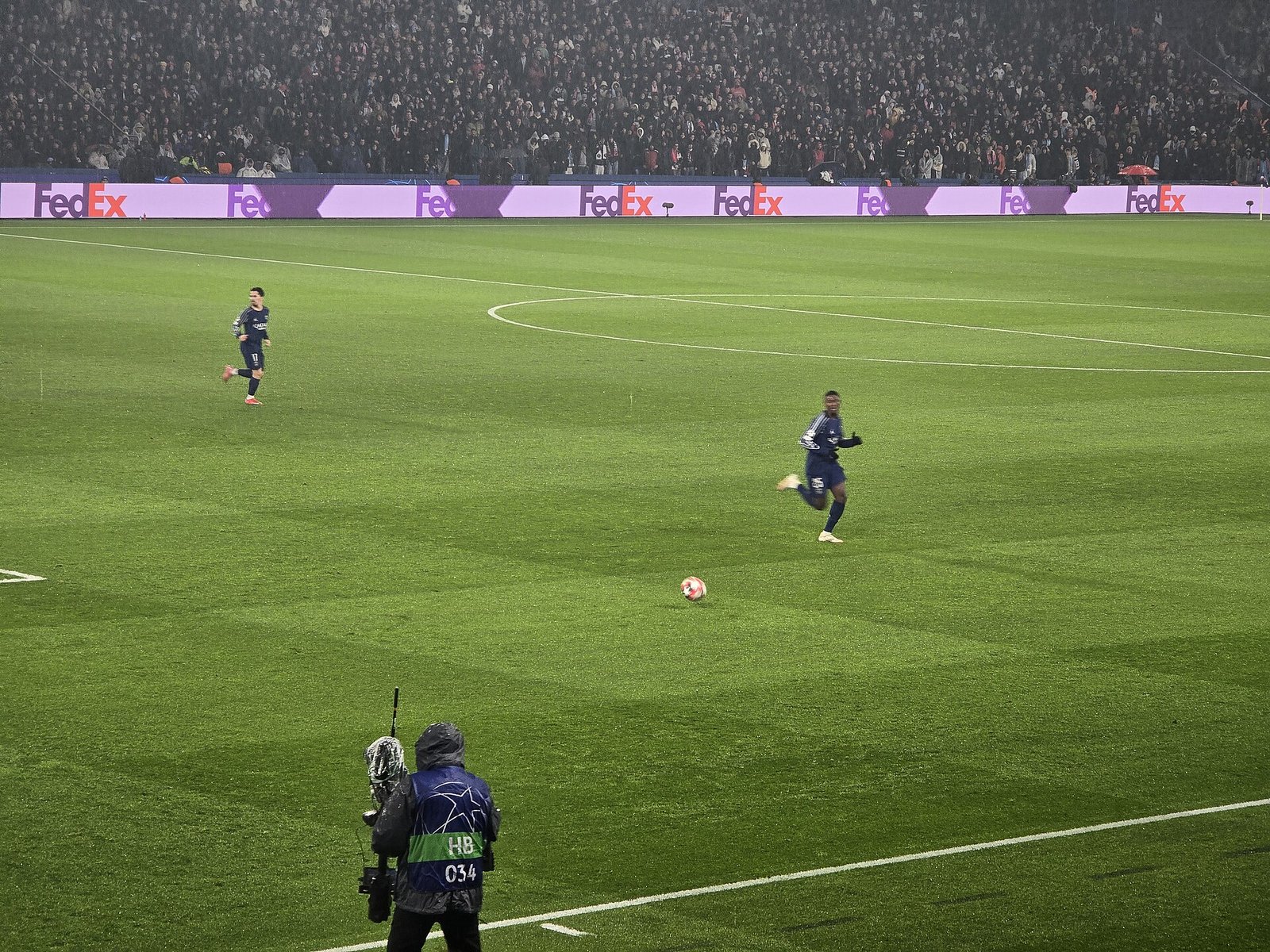 Joueur du PSG en course vers le ballon sur la pelouse, caméraman UEFA au premier plan, tribunes en fond