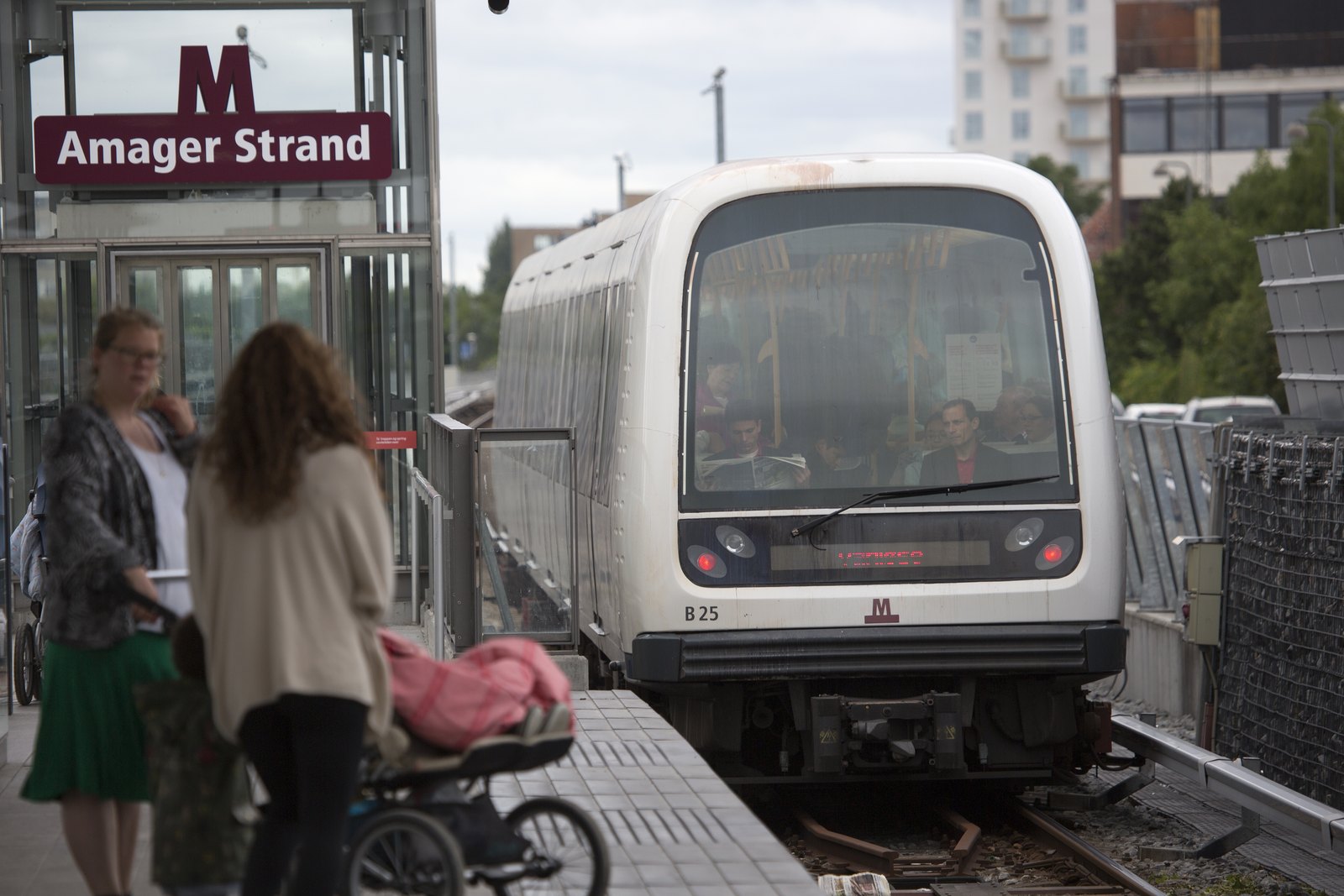 Voyageurs, dont une mère avec une poussette, attendant une rame du métro automatique à la station aérienne Amager Strand